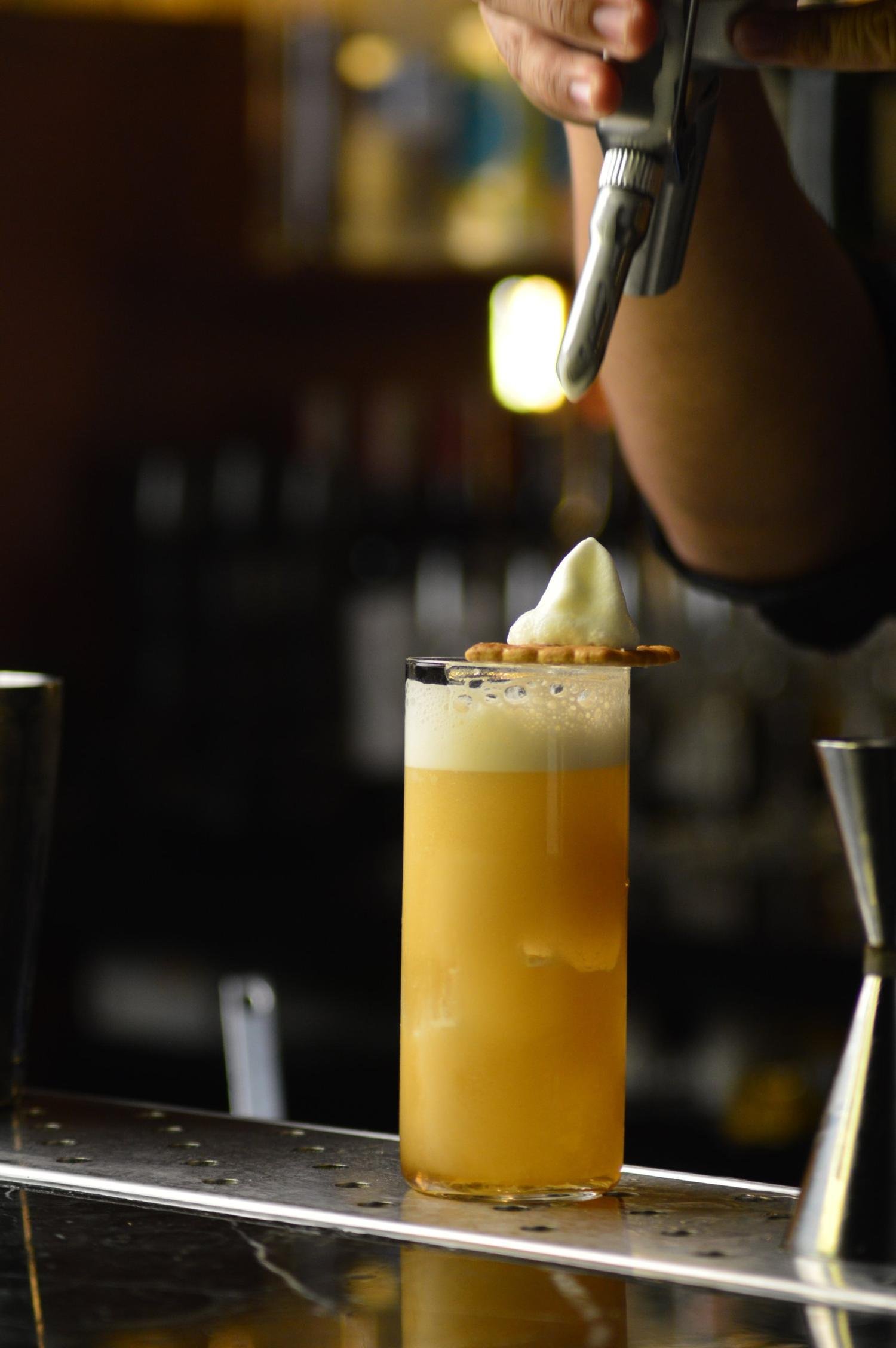 A foamy orange cocktail topped with cream at a dark bar